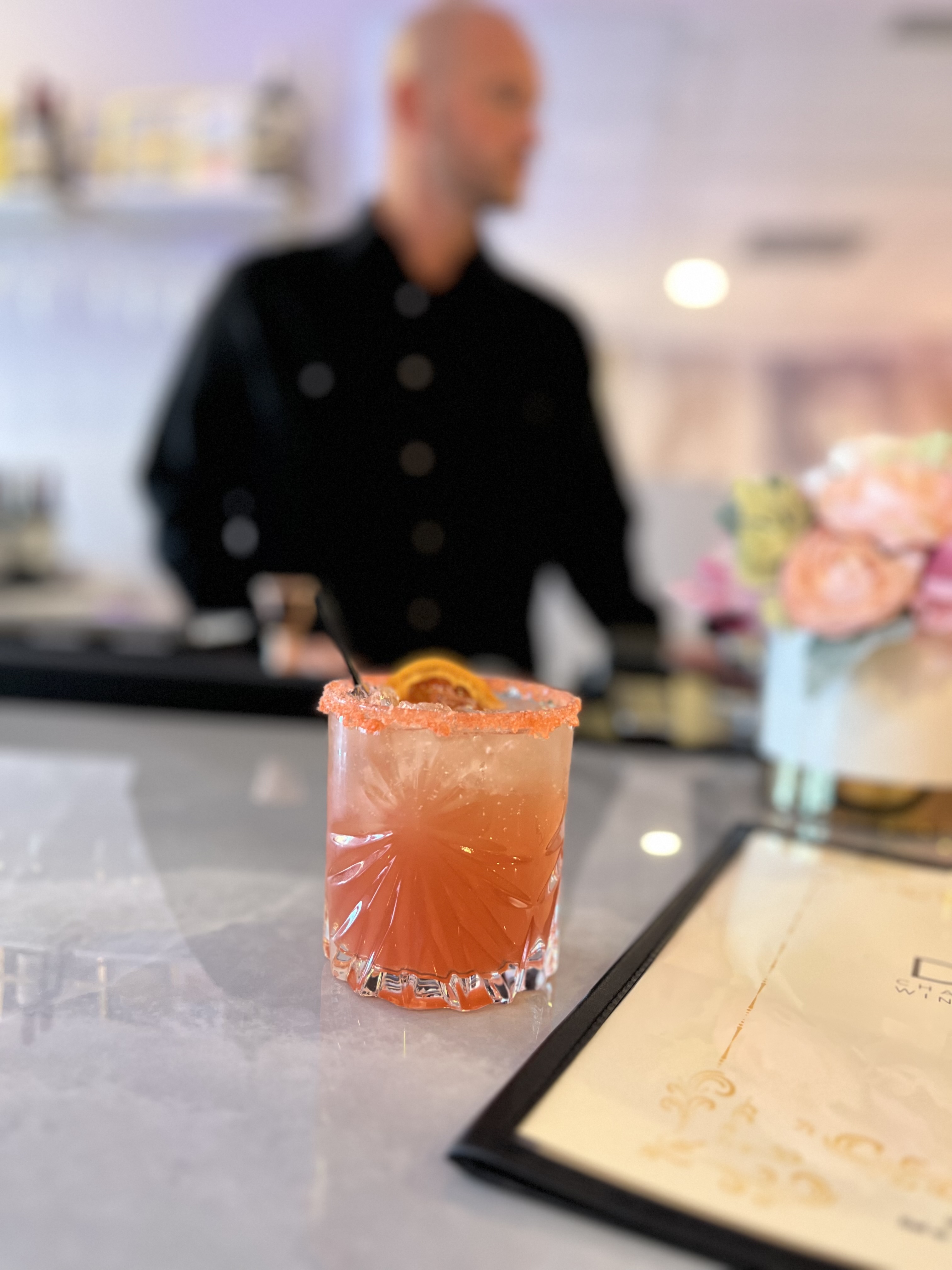 citrus coctail next to the menu with a bartender in the background