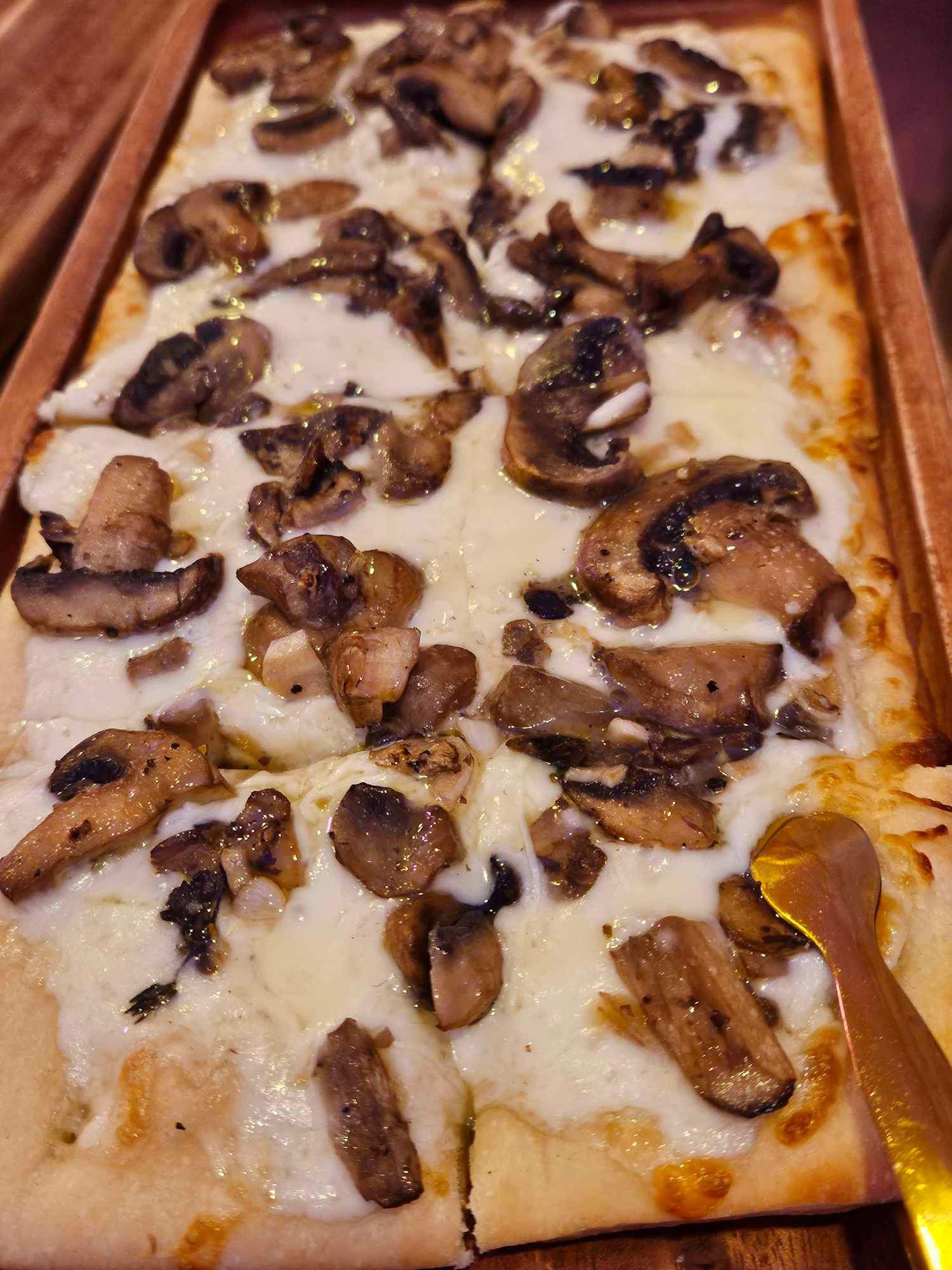 mushroom and cheese flatbread on wood board with gold serving tongs