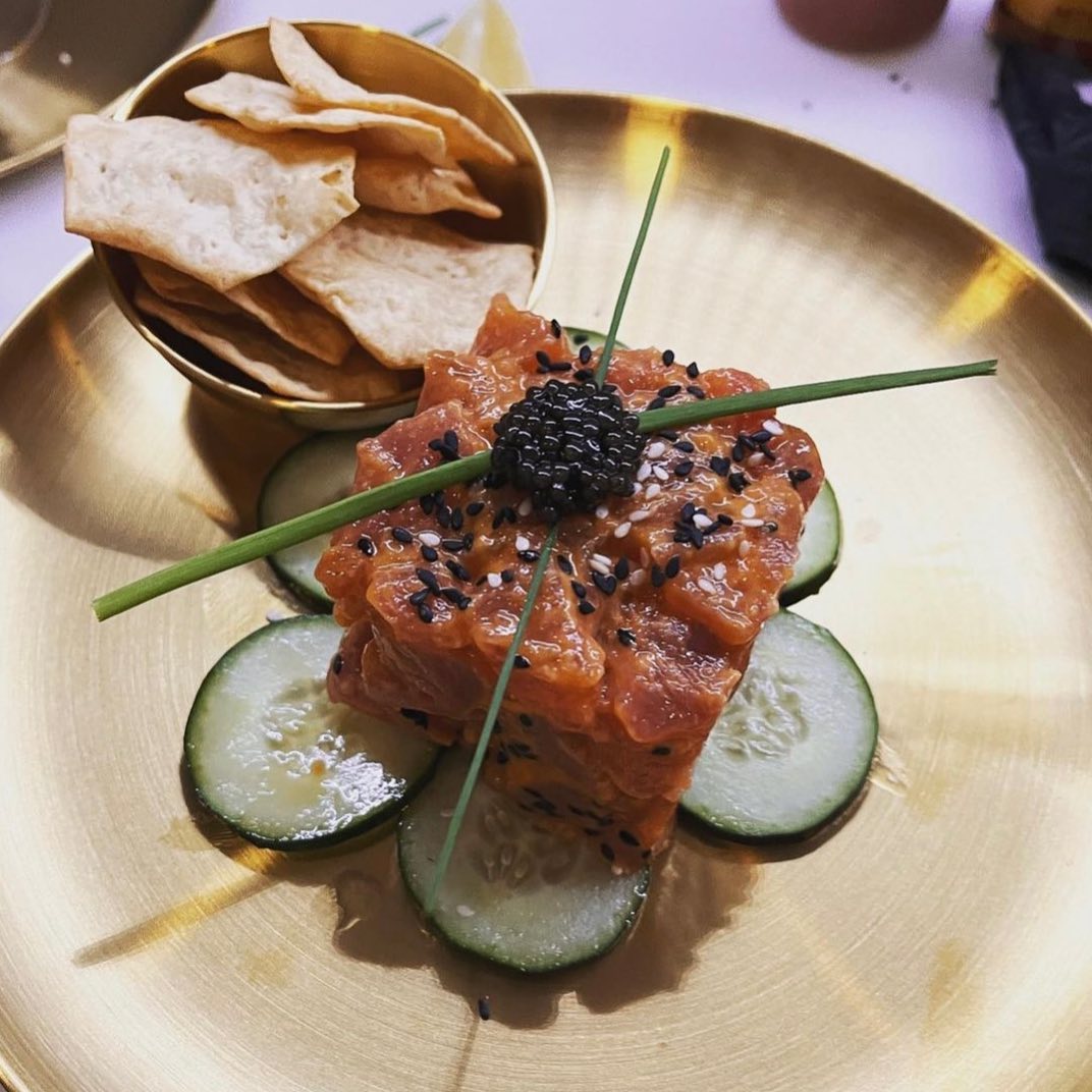 tuna tartare on a bed of sliced cucumbers topped with caviar on a gold plate 